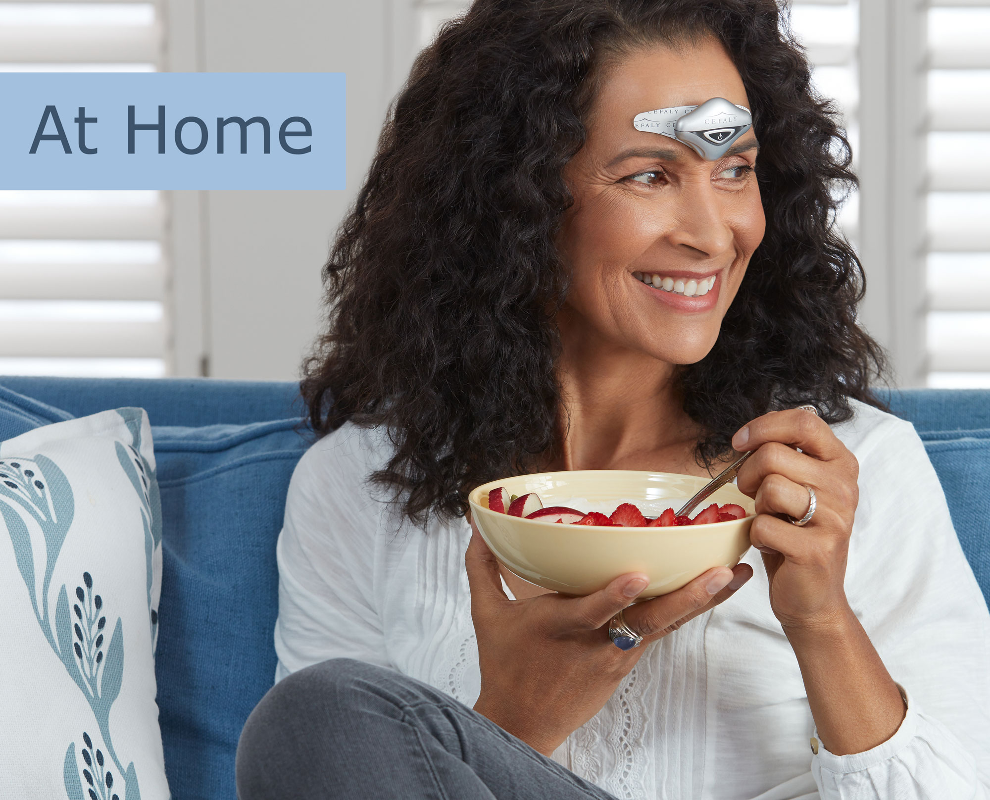 Woman eating on a couch while using her Cefaly device to prevent and treat her migraines