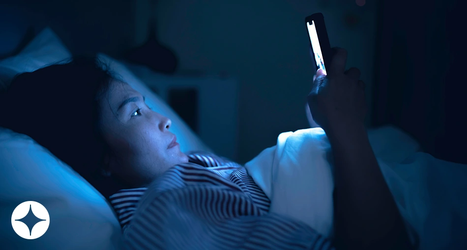 A woman in bed looking at her cell phone in the dark.