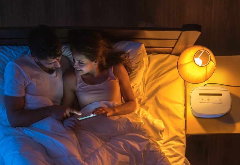 A couple laying down in bed next to a SoClean 3 on the nightstand